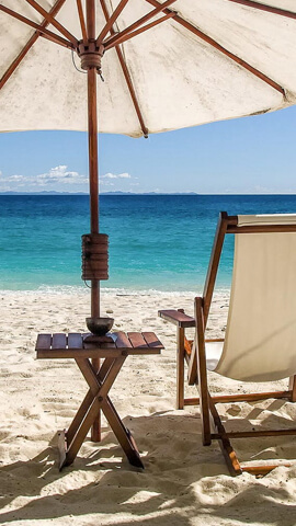 A recliner chair under the shade of a canopy, in beach, with a view of the sea